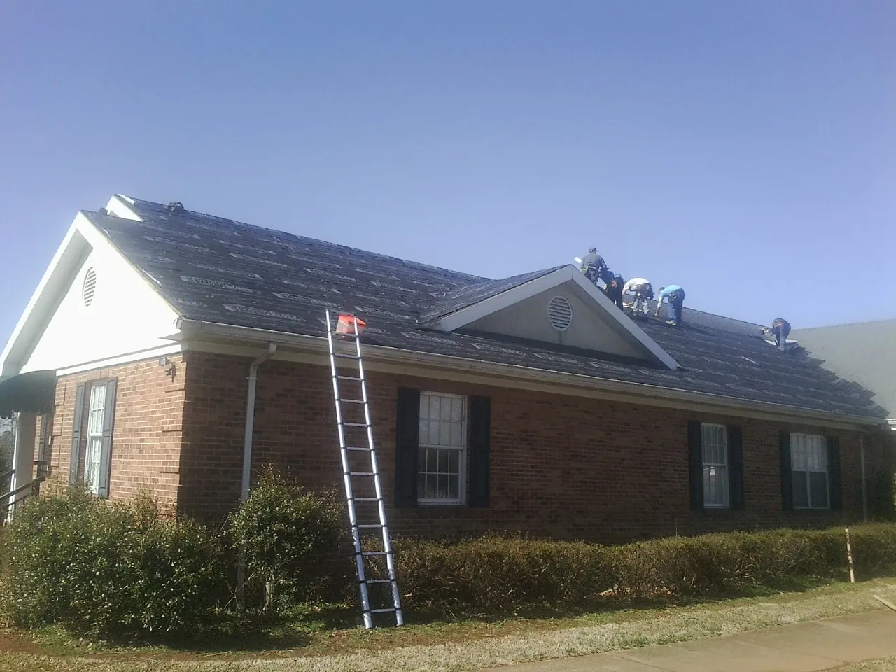 Crew tearing shingles off a brick ranch roof with a ladder set — Emergency Roof Repair work by our crew in Bangor