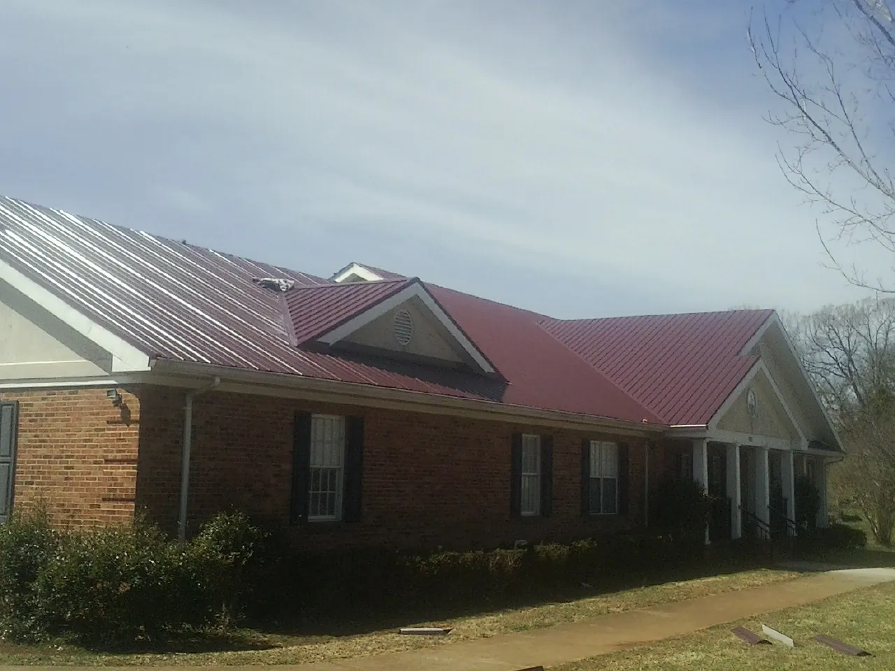 Red metal roof with gabled entries on a long brick building, from a Hail Damage Roof Repair job in Bangor