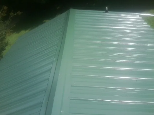 New green metal panels meeting at the ridge of a roof — Flat Roof Repair work by our crew in Bangor