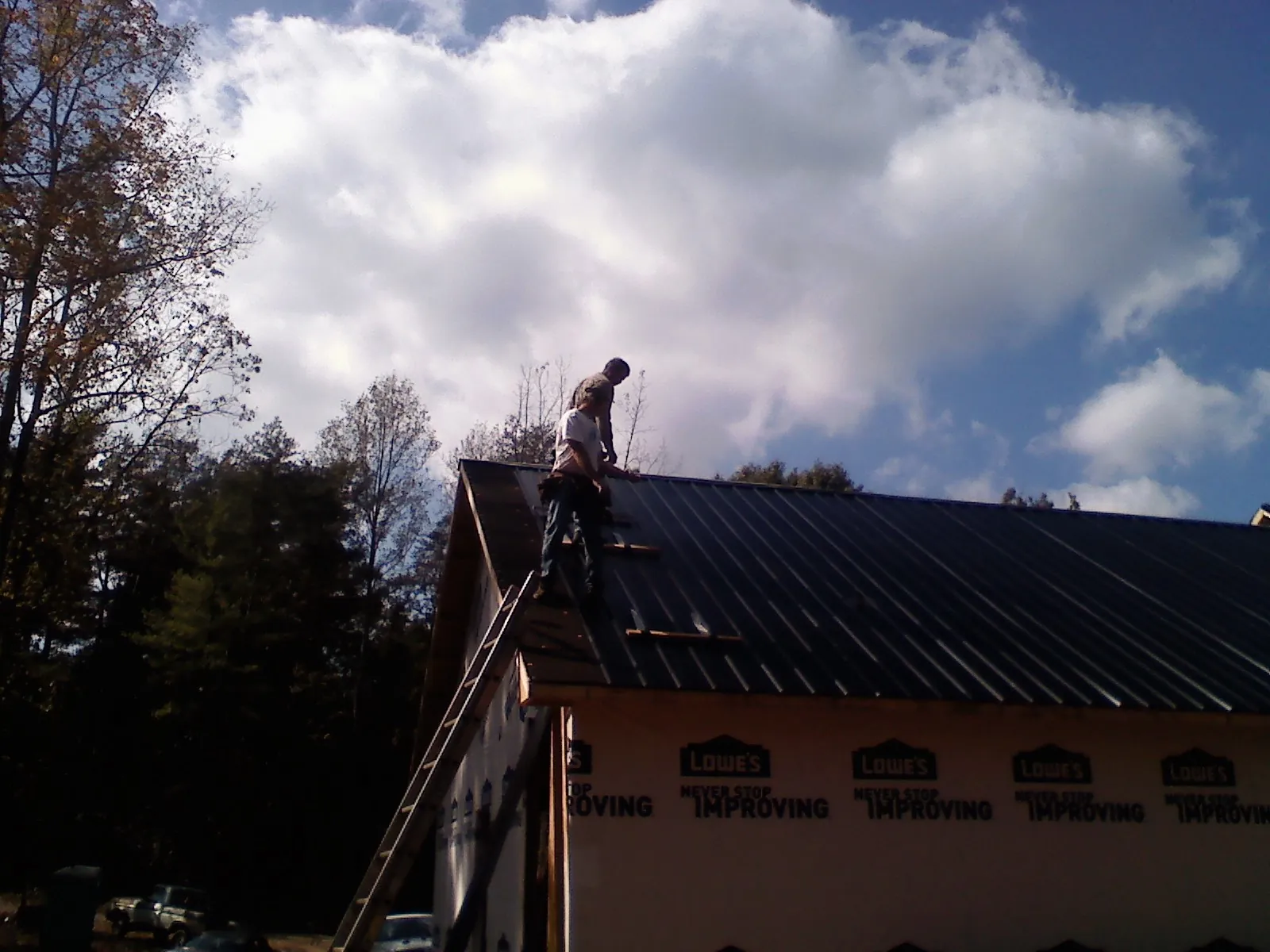 Roofer fastening dark metal panels high against a cloudy sky, from a Roof Inspection job in Bangor