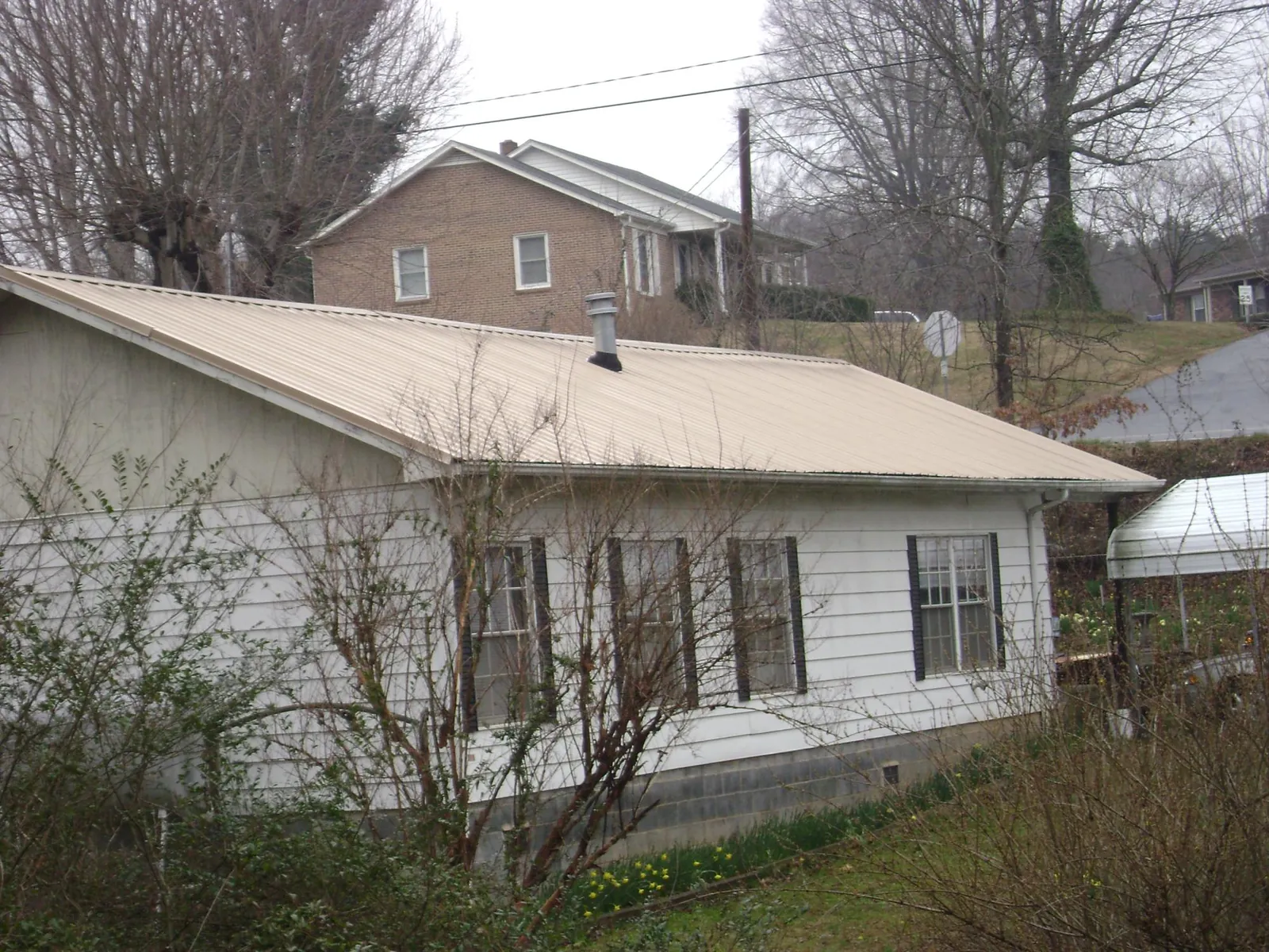 Tan metal roof on a white sided house set into a hillside — Commercial Roofing by Roofing Brothers in Bangor