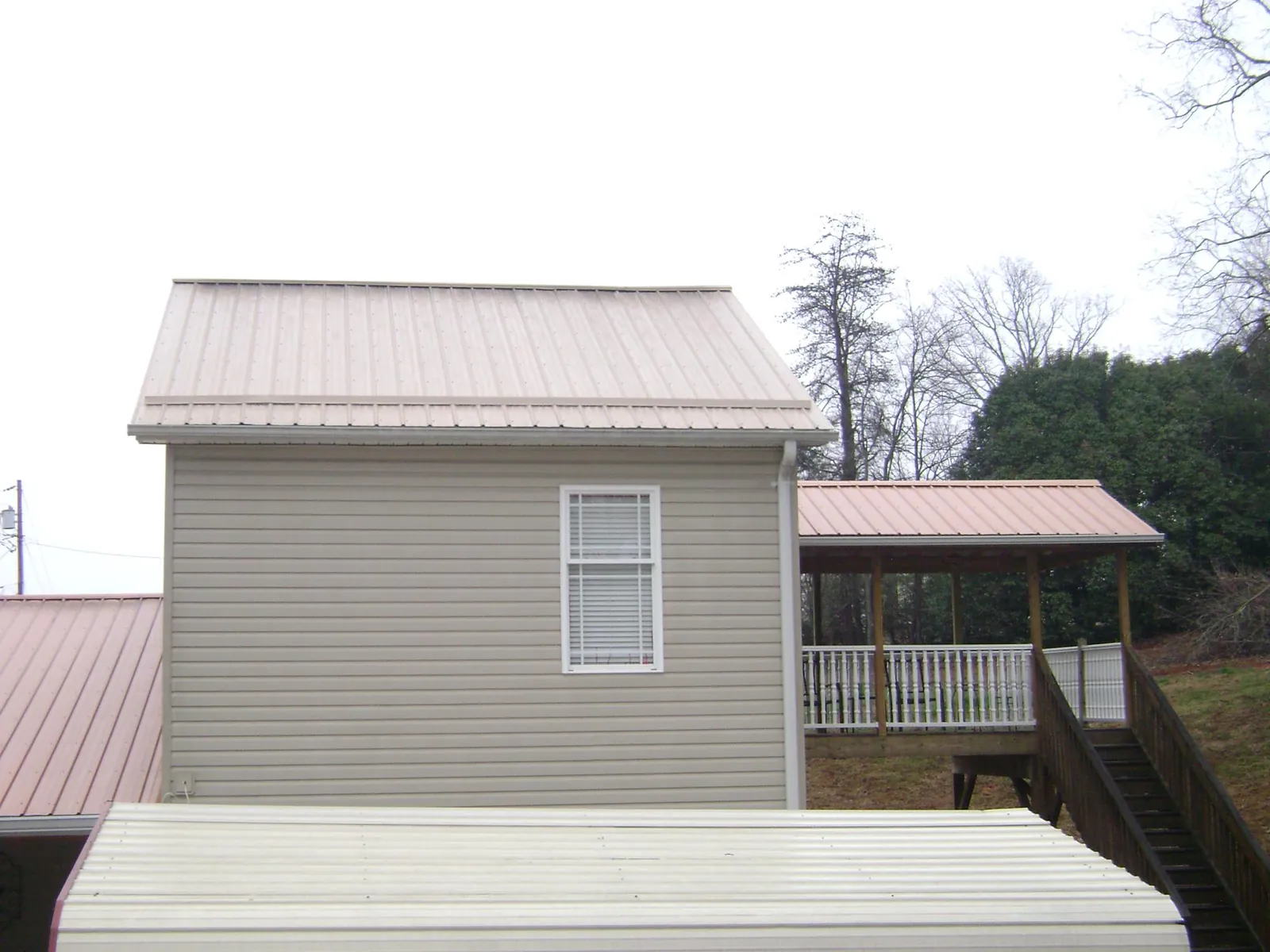 Tan metal roofs on a two story addition and attached porch, from a Roof Replacement job in Bangor